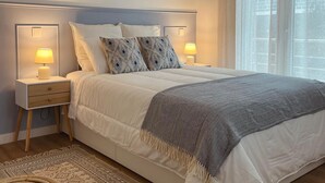 Een slaapkamer met een bed, nachtlampjes, een vloerkleed, een stoel en een airconditioner.