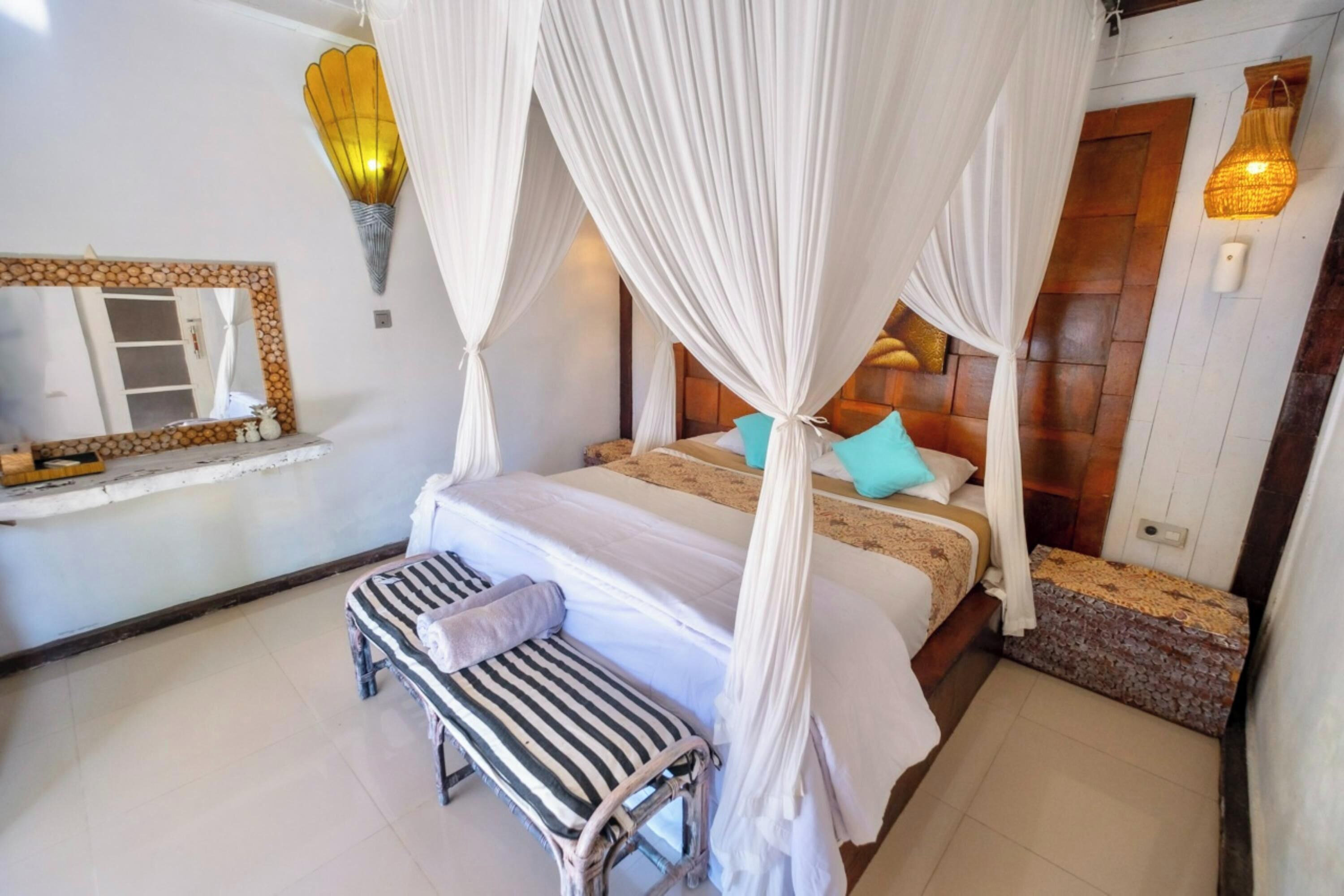 A bedroom with a bed, a bench, a bedside table, a mirror, and a wall-mounted light fixture.