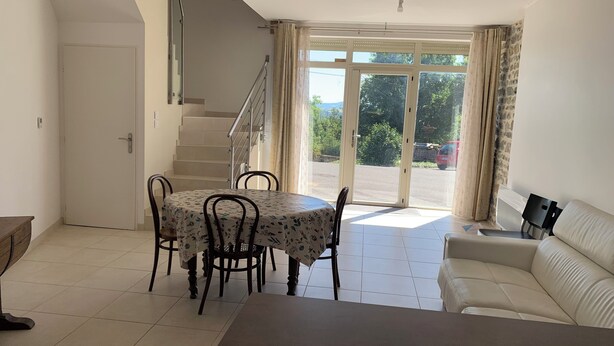 A dining area with a table and chairs, a sofa, a staircase, and a view through a glass door. - GITE in the countryside, fully renovated, 30 mn from Lyon, near l'Arbresle (Savigny)