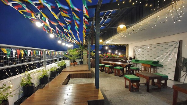 A restaurant with wooden tables and chairs, a bar area with stools, and a ceiling adorned with colorful flags and string lights. - Teofel Hostel by Hiverooms (Cebu City)