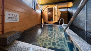 Un onsen japonais traditionnel, avec un intérieur en bois et un bassin en pierre à l’eau claire.