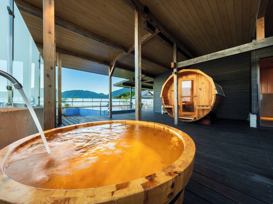 A wooden hot tub on a deck with a view of mountains.