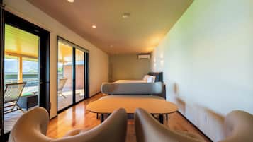 A modern room with a sofa, a small table, and a chair. There is a sliding glass door leading to an outdoor area with a chair.