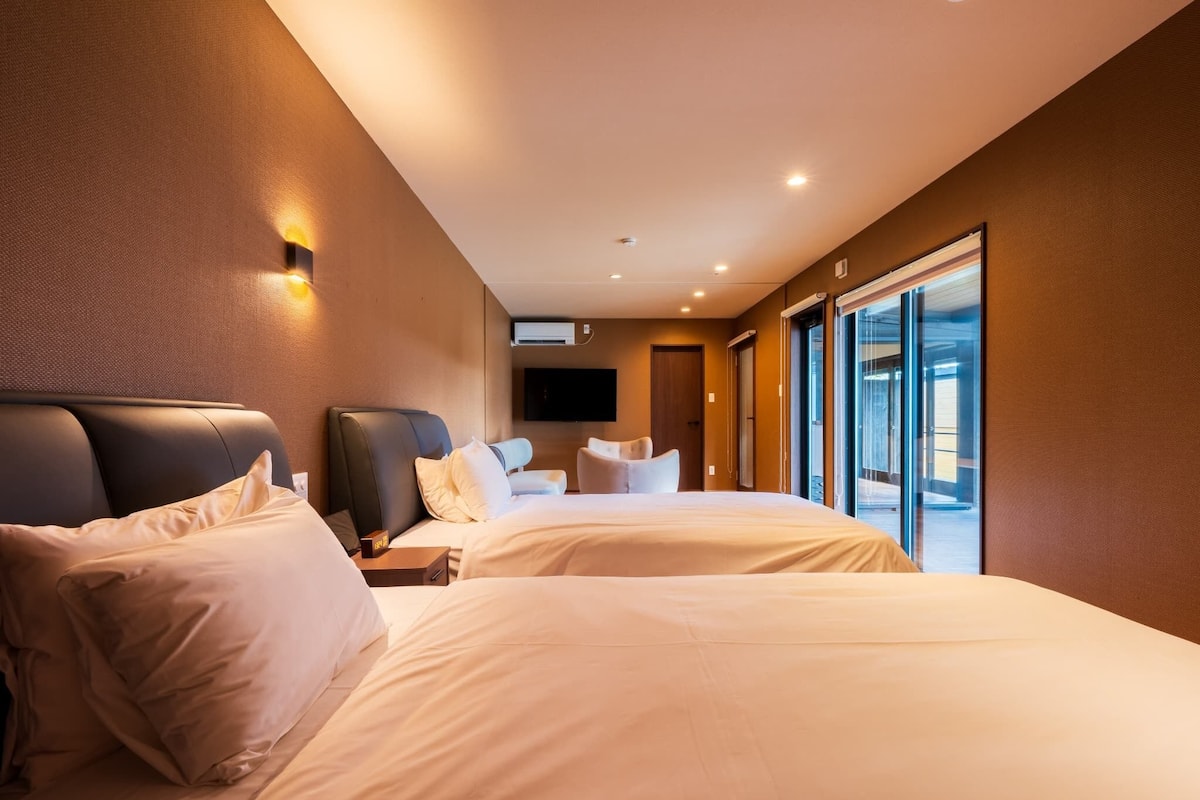 Une chambre d’hôtel moderne, dotée de deux lits, d’une grande fenêtre et d’un téléviseur à écran plat fixé au mur.