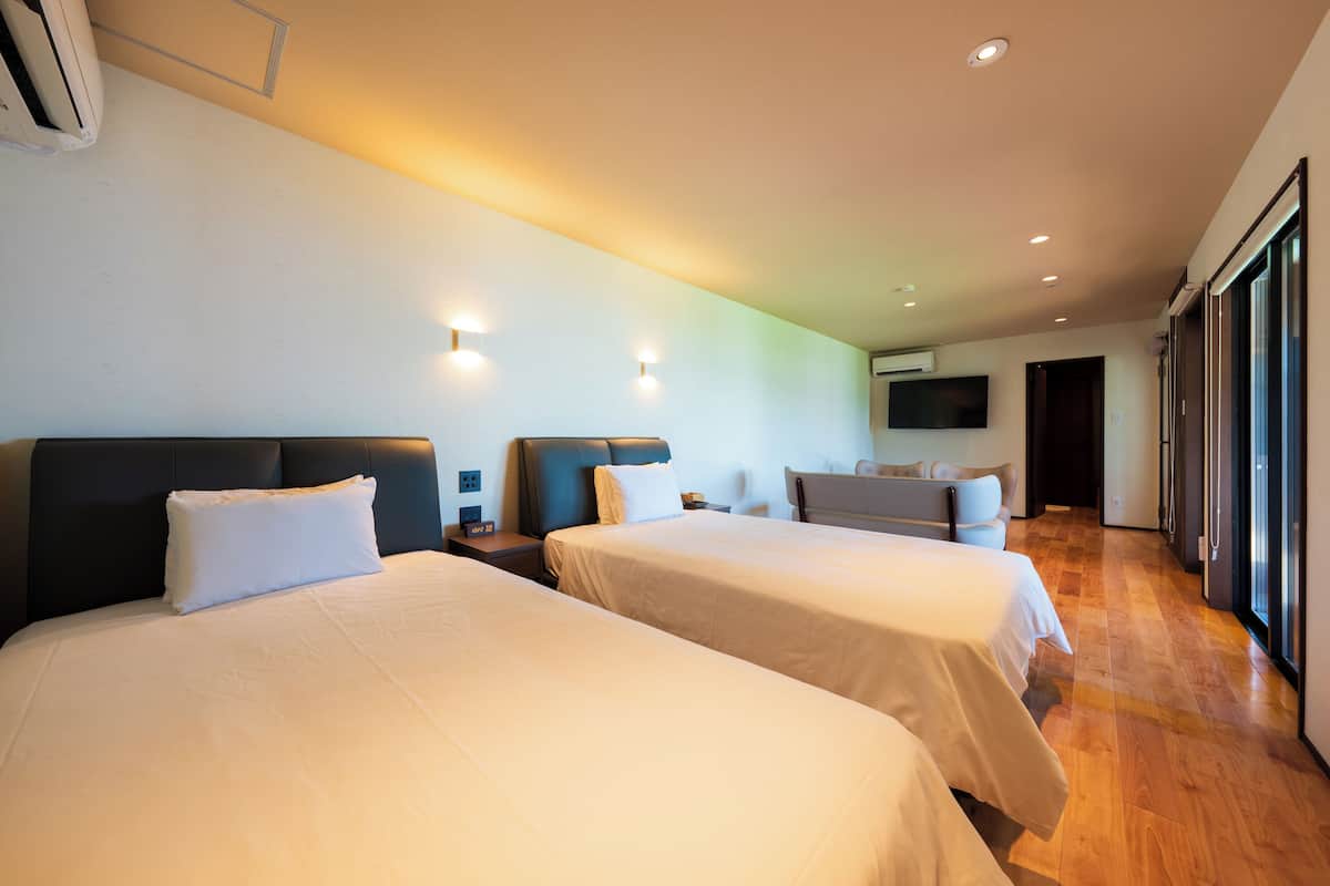 Une chambre d’hôtel avec deux lits, un canapé, une télévision et une grande fenêtre.
