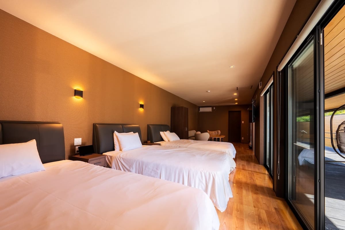 Une chambre d’hôtel avec deux lits, un petit coin salon et une grande porte-fenêtre coulissante donnant sur un espace extérieur.
