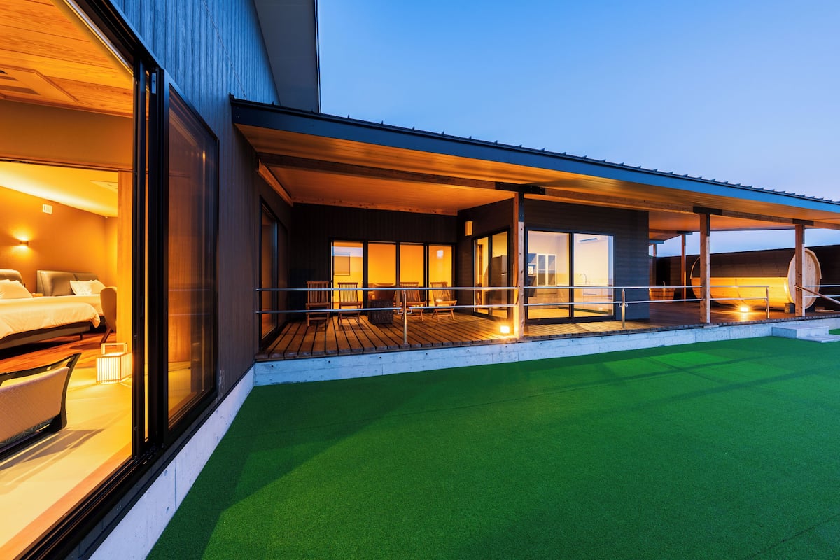 Un hôtel moderne doté d’un espace extérieur couvert, d’une pelouse verdoyante et d’une grande fenêtre donnant sur l’intérieur.