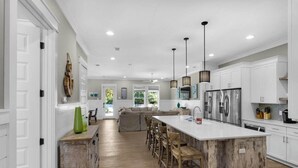 Una cocina moderna con armarios blancos, una isla central con taburetes y electrodomésticos de acero inoxidable.