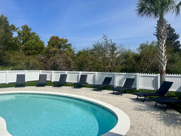 A swimming pool with lounge chairs and a white picket fence.