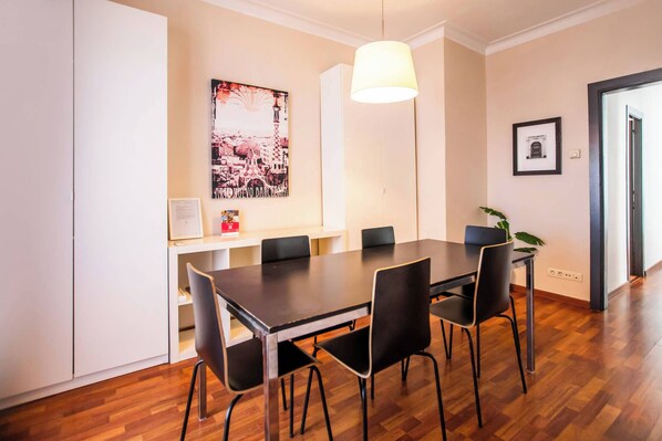 A dining area with a long table, black chairs, a hanging light fixture, and a framed picture on the wall.