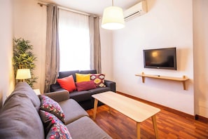 Uma sala de estar moderna com um sofá, uma mesa de centro, uma TV em uma prateleira na parede e um vaso de planta.