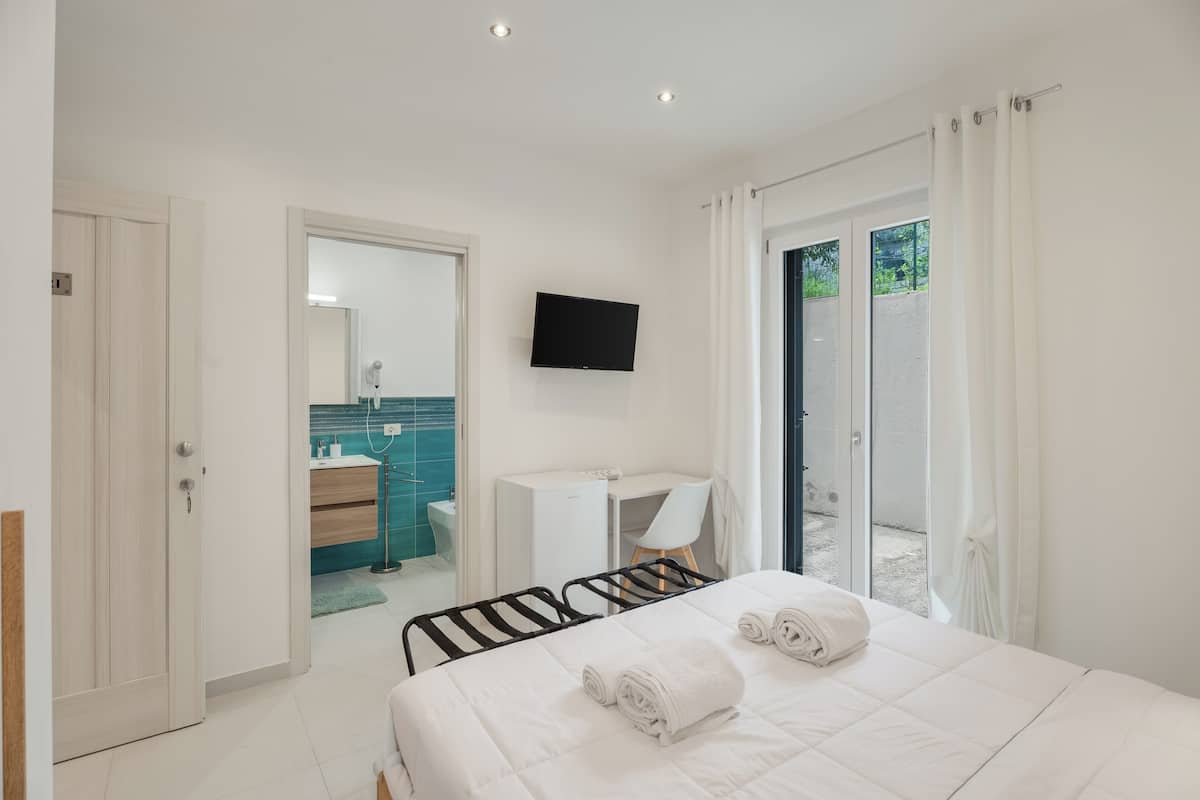 Une chambre d’hôtel avec un lit, un bureau, une télévision et une salle de bain visible à travers une porte ouverte.