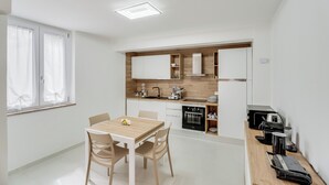 A modern kitchen with white cabinets, a dining table with chairs, and a coffee machine. - B&B Santa Maria (Agerola)