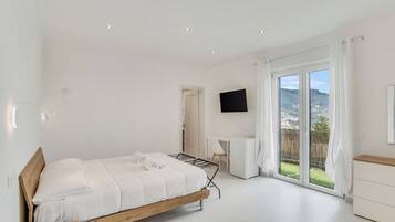 Un dormitorio moderno con cama, escritorio, televisor y puerta corrediza de cristal a un balcón.