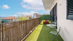 A balcony with artificial grass, a table, chairs, and a planter with flowers. - B&B Santa Maria (Agerola)