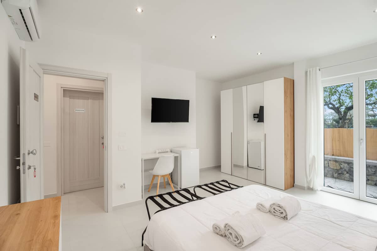 Une chambre moderne comprenant un lit, un bureau, une chaise, un téléviseur et une porte-fenêtre coulissante donnant sur l’extérieur.