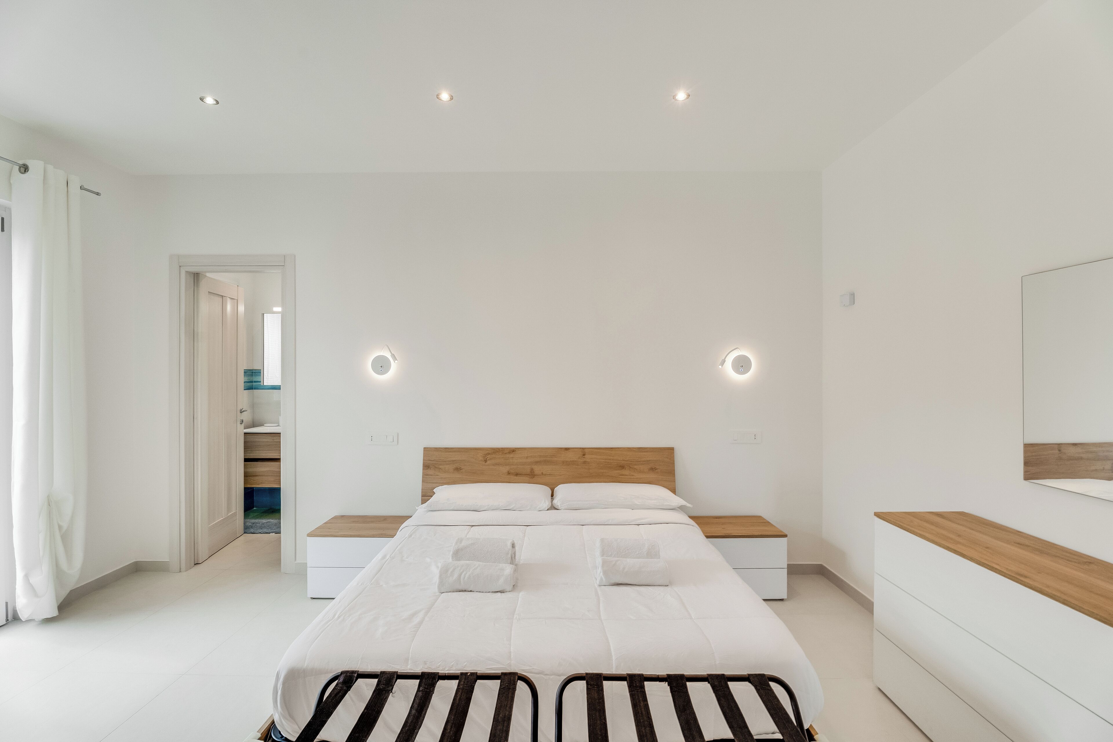 Un dormitorio moderno con una cama grande, mesitas de noche, un cabecero de madera y un espejo en la pared.
