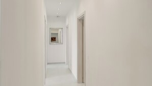 A corridor with white walls, a tiled floor, recessed lighting, and a door at the end. - B&B Santa Maria (Agerola)