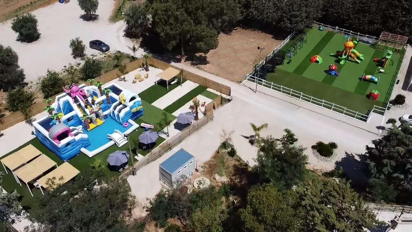 Eine Vogelperspektive auf ein Anwesen mit Schwimmbad, Hüpfburg und eingezäuntem Sportplatz.