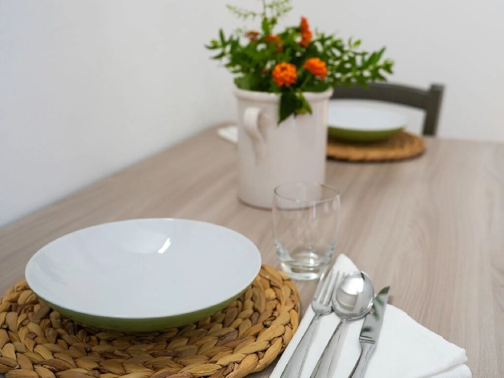 Uma mesa de jantar com um prato branco, um copo transparente e talheres sobre um jogo americano de tecido.