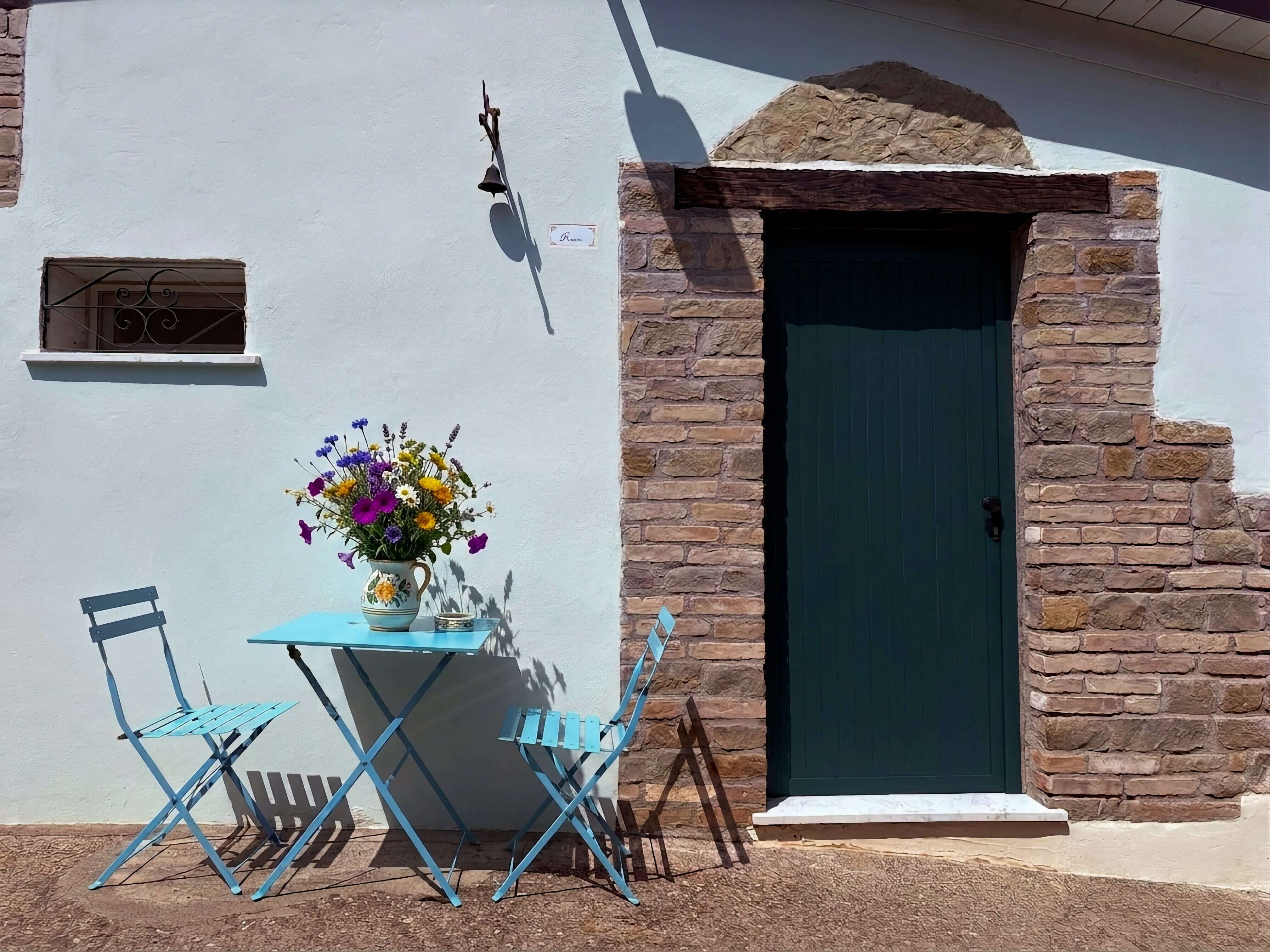A room with a stone wall, a green door, a small window, and a table with chairs.