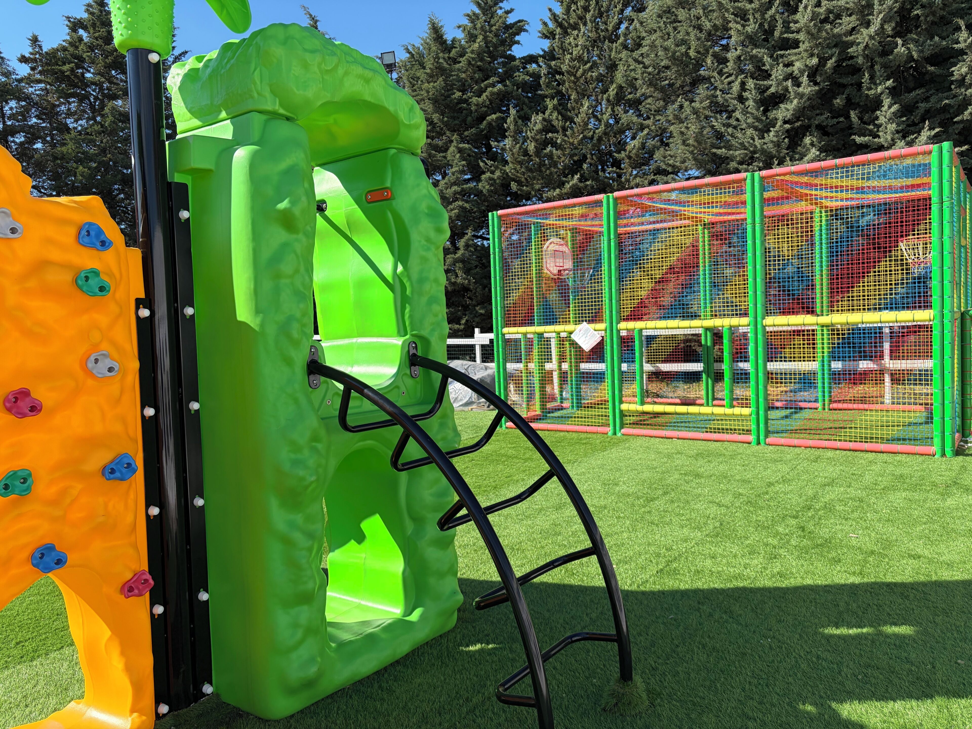 A playground with a climbing wall, a slide, and a netted play area.