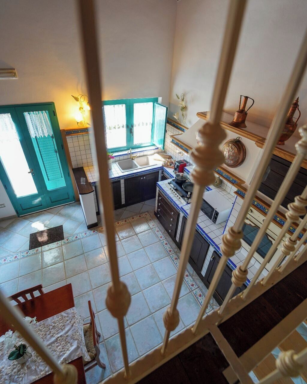 Cocina con estufa, lavabo y armarios. Hay una ventana con cortinas y una puerta con marco verde.