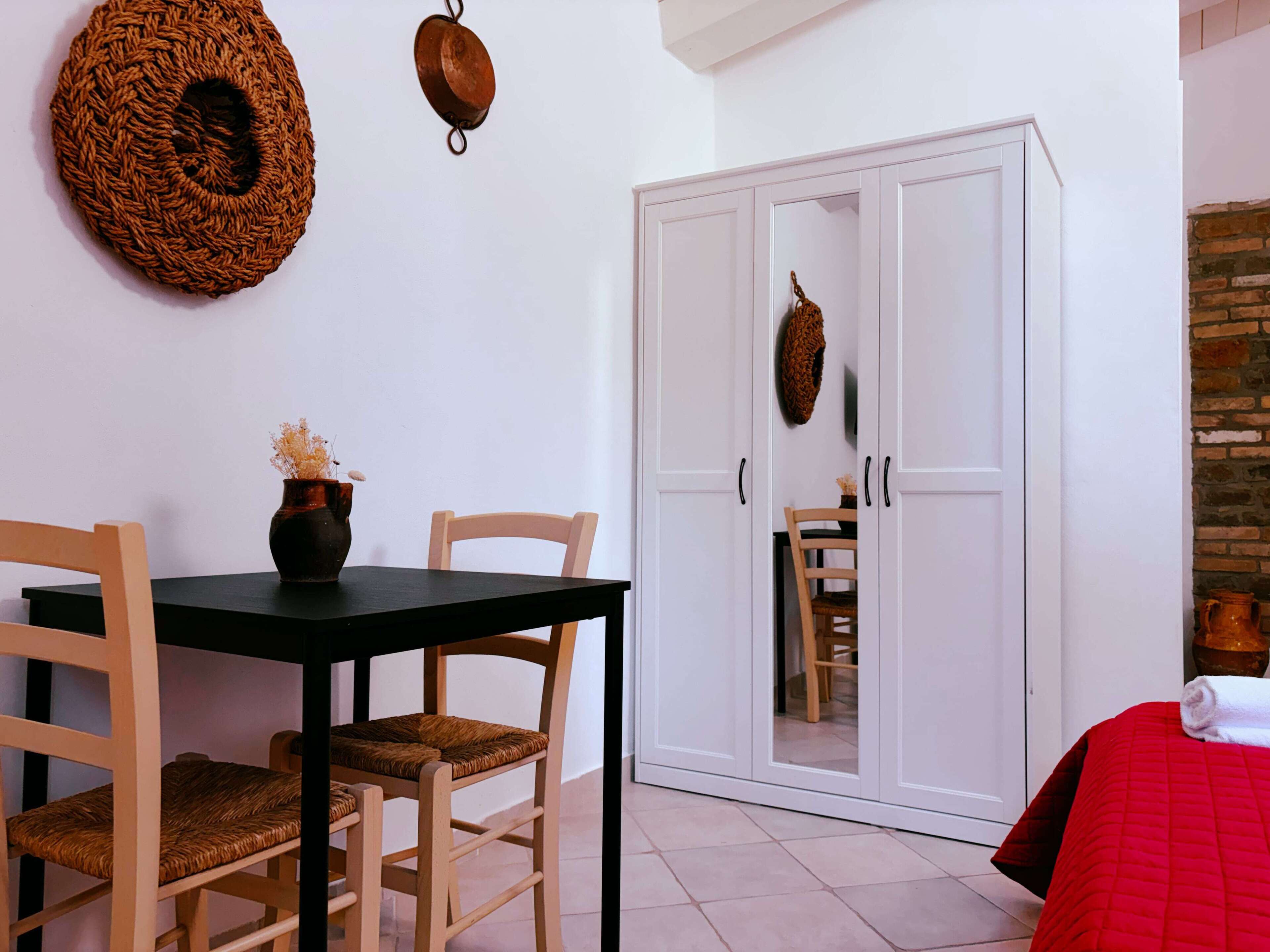 Una habitación con una mesa de comedor, sillas, un armario y una cama con una colcha roja.