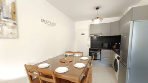 A modern kitchen with stainless steel appliances, a dining area with wooden chairs and a table set for four, and a 'BIENVENUE' sign on the wall. - T2 with garden and parking, 6 ppl - Saint-Lary-Soulan (Saint-Lary-Soulan)
