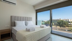 A modern bedroom with a large bed, a nightstand, and a view of a cityscape through a large window. - Rodos Stars Stellar Villas - Leontas (Rhodes)