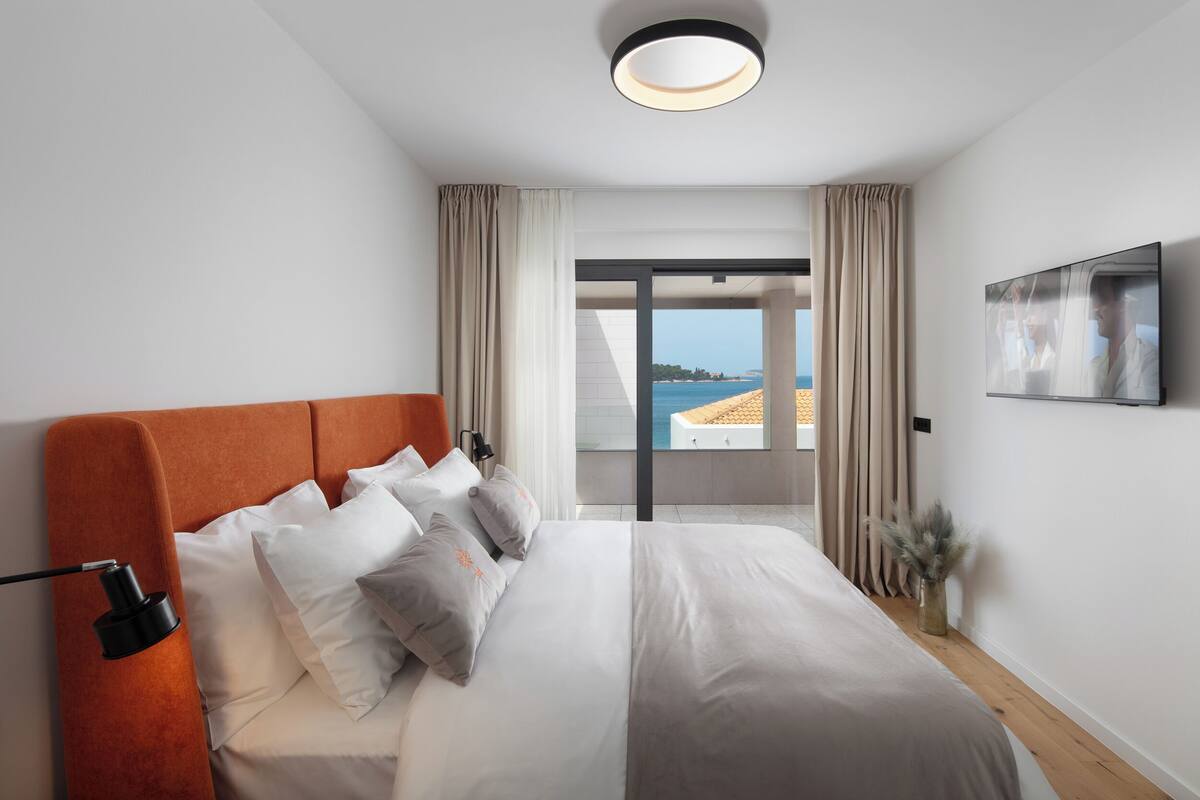 A modern hotel room with a large bed, a flat-screen TV, and a balcony with a view of the sea.