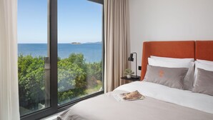 Habitación de hotel con un ventanal grande que ofrece vistas al mar y al verdor.
