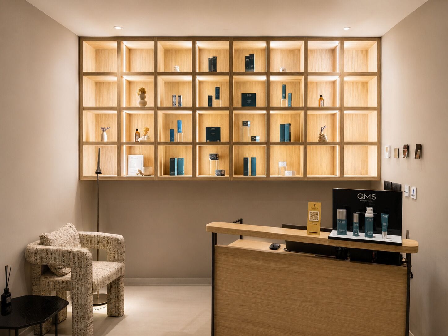 Una recepción con un cartel de QMS, una estantería de madera con diversos objetos y un sillón estampado.