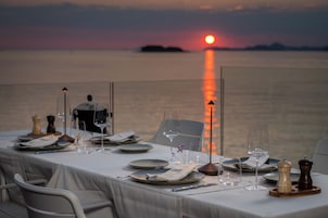 Mesa lista para una comida con vista a la puesta de sol sobre el agua.