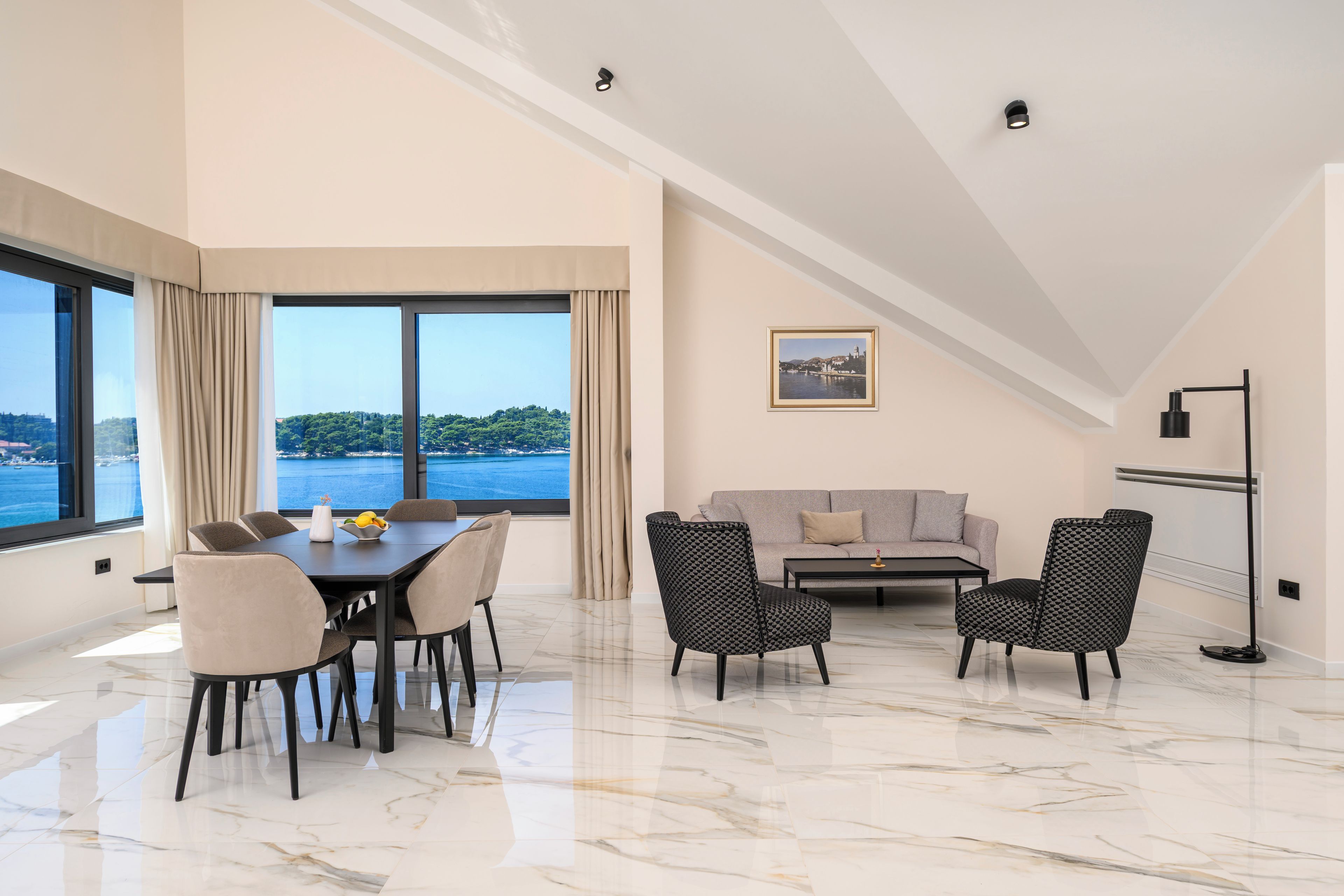 Una sala de estar moderna con comedor, ventanas amplias con vista al mar, un sofá y una lámpara de pie.