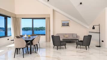 Una sala de estar moderna con comedor, ventanas amplias con vista al mar, un sofá y una lámpara de pie.