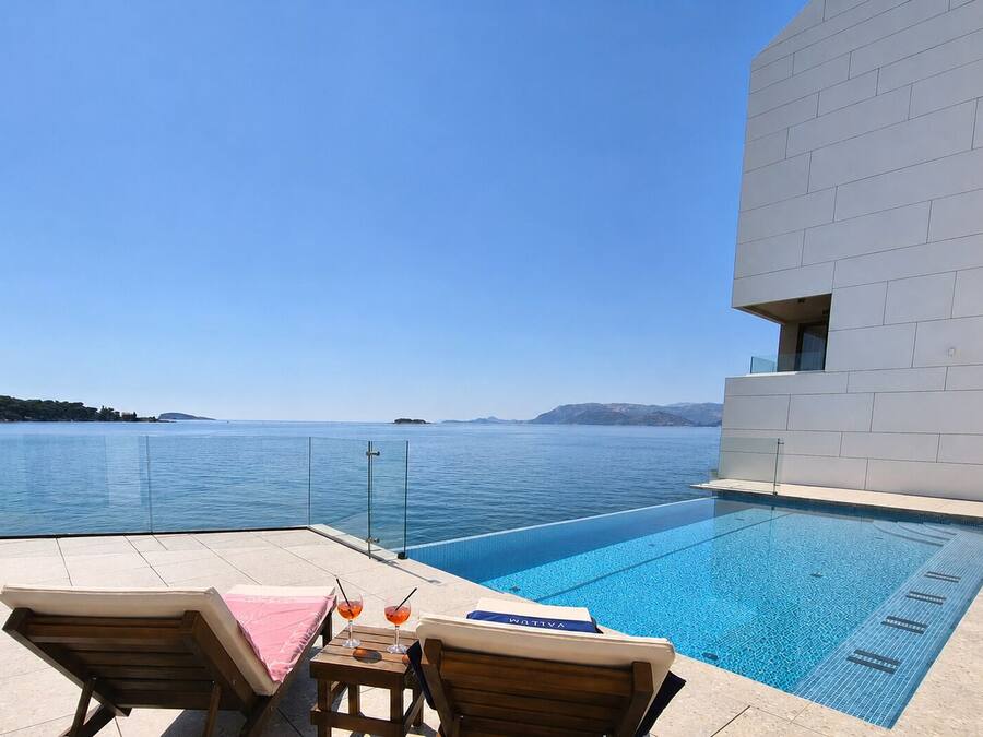 Zona de piscina con sillones de descanso, una mesa con bebidas y vista al mar.