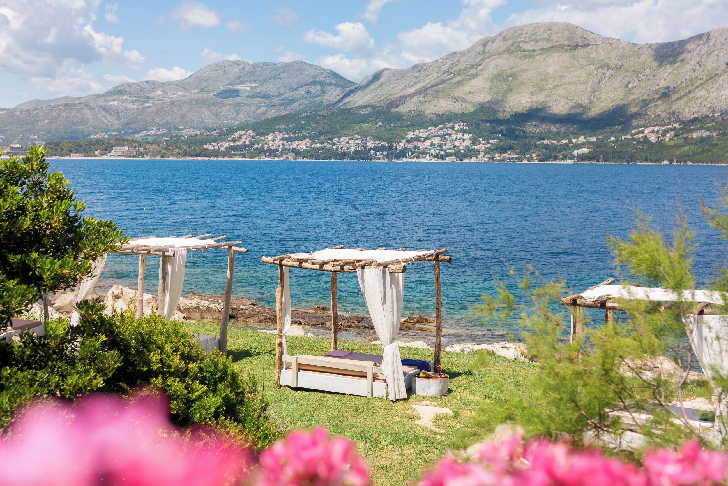 A lakeside setting with wooden structures, possibly for outdoor dining or relaxation, overlooking a calm lake and distant mountains.