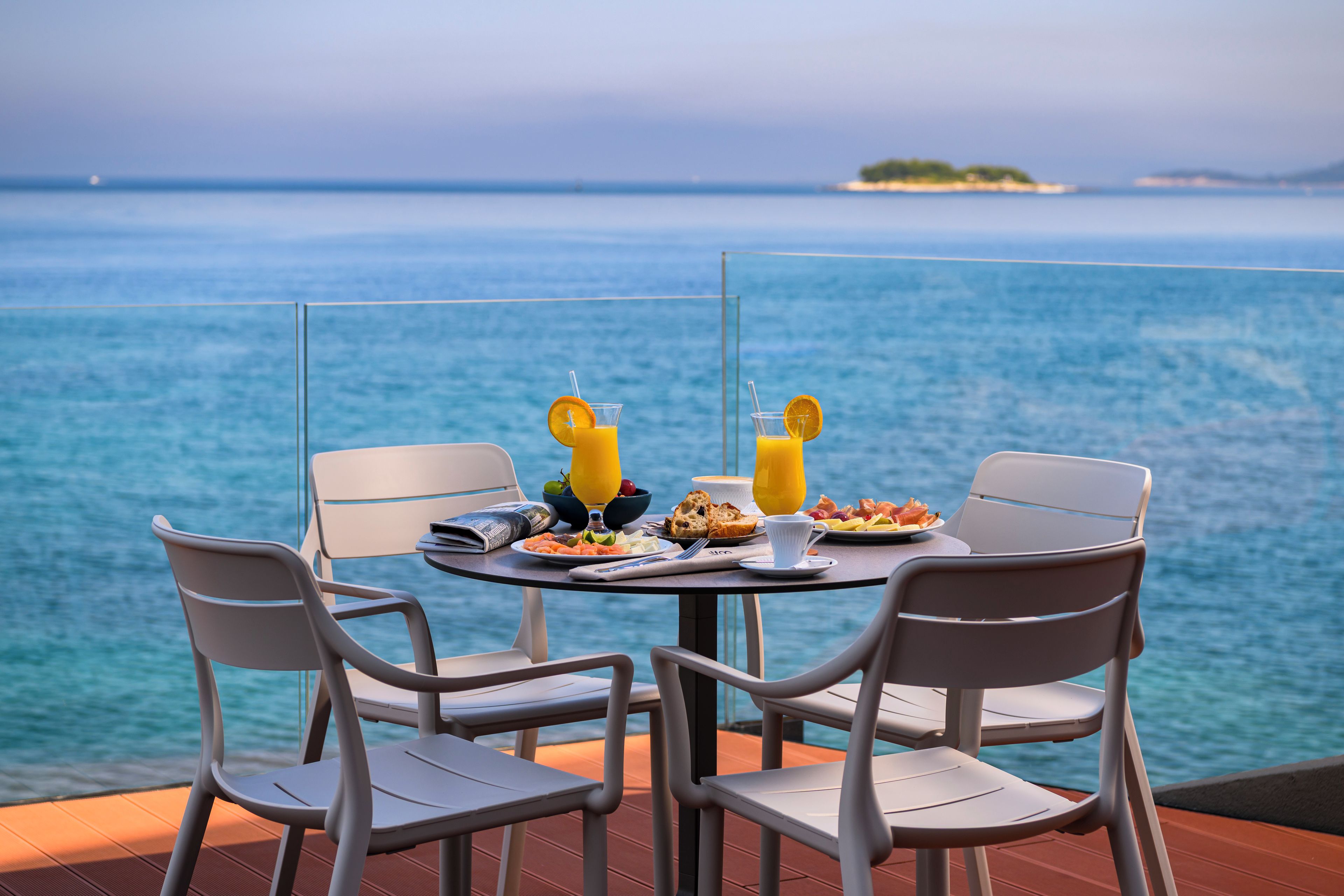 Une table dressée avec des aliments pour le petit-déjeuner et un verre de jus d’orange, donnant sur une étendue d’eau.