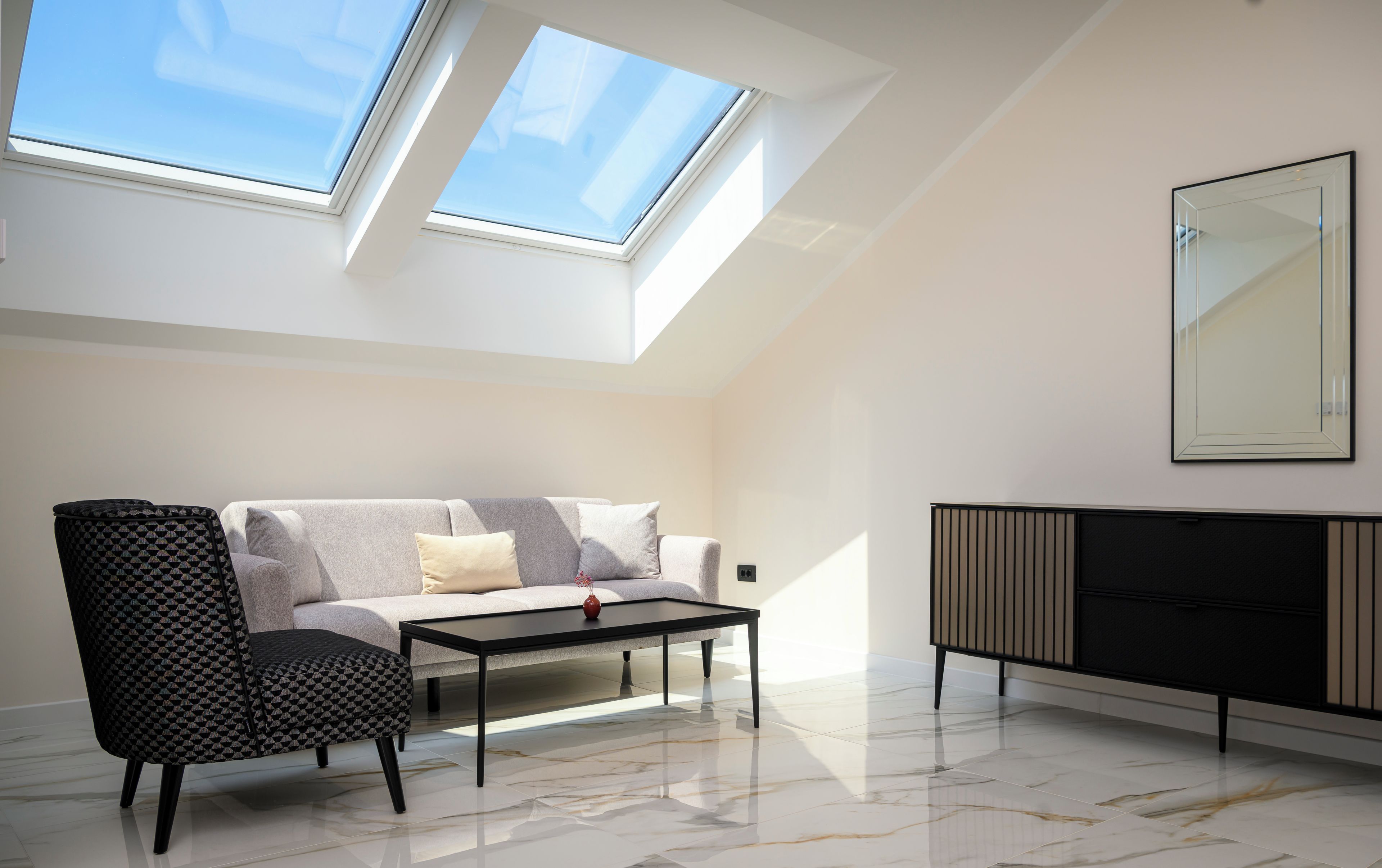 Una sala de estar moderna con sofá, reposapiés, mesa de centro y un mueble. Hay tragaluces que proporcionan luz natural.