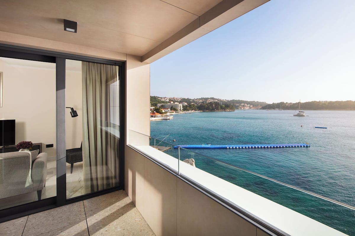 A balcony with a glass door, a dining area with a table and chairs, and a view of the sea with boats and a distant shoreline.