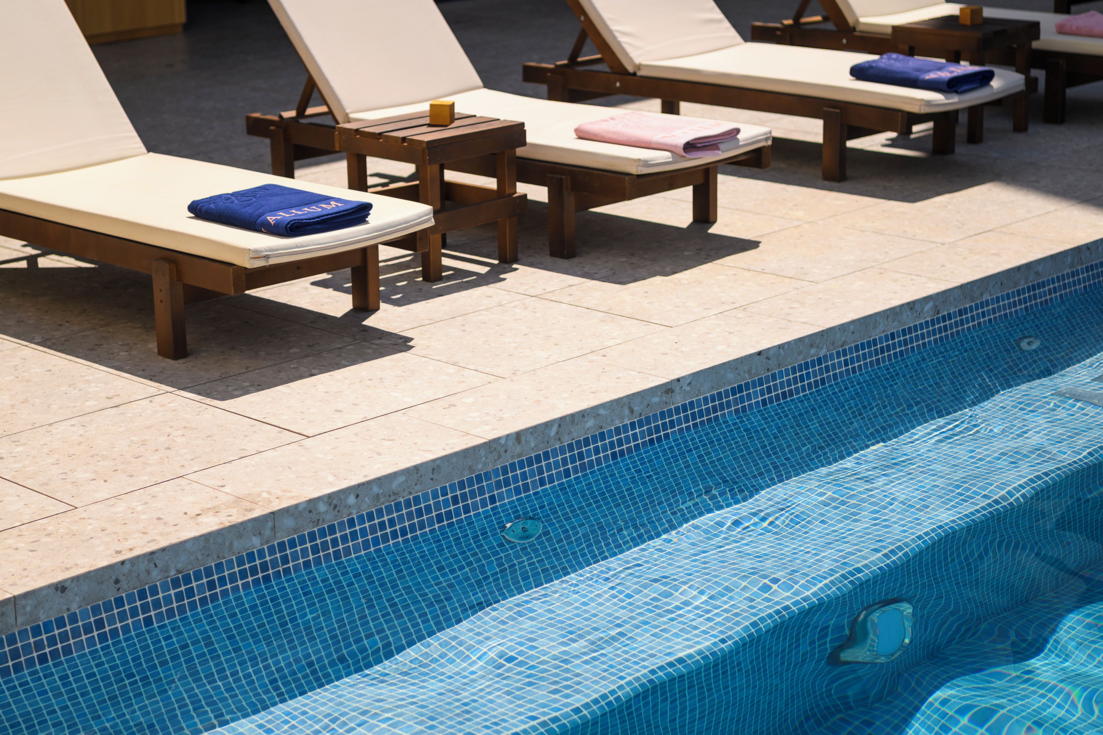 Zona junto a la piscina con sillones de descanso y una piscina con baldosas.