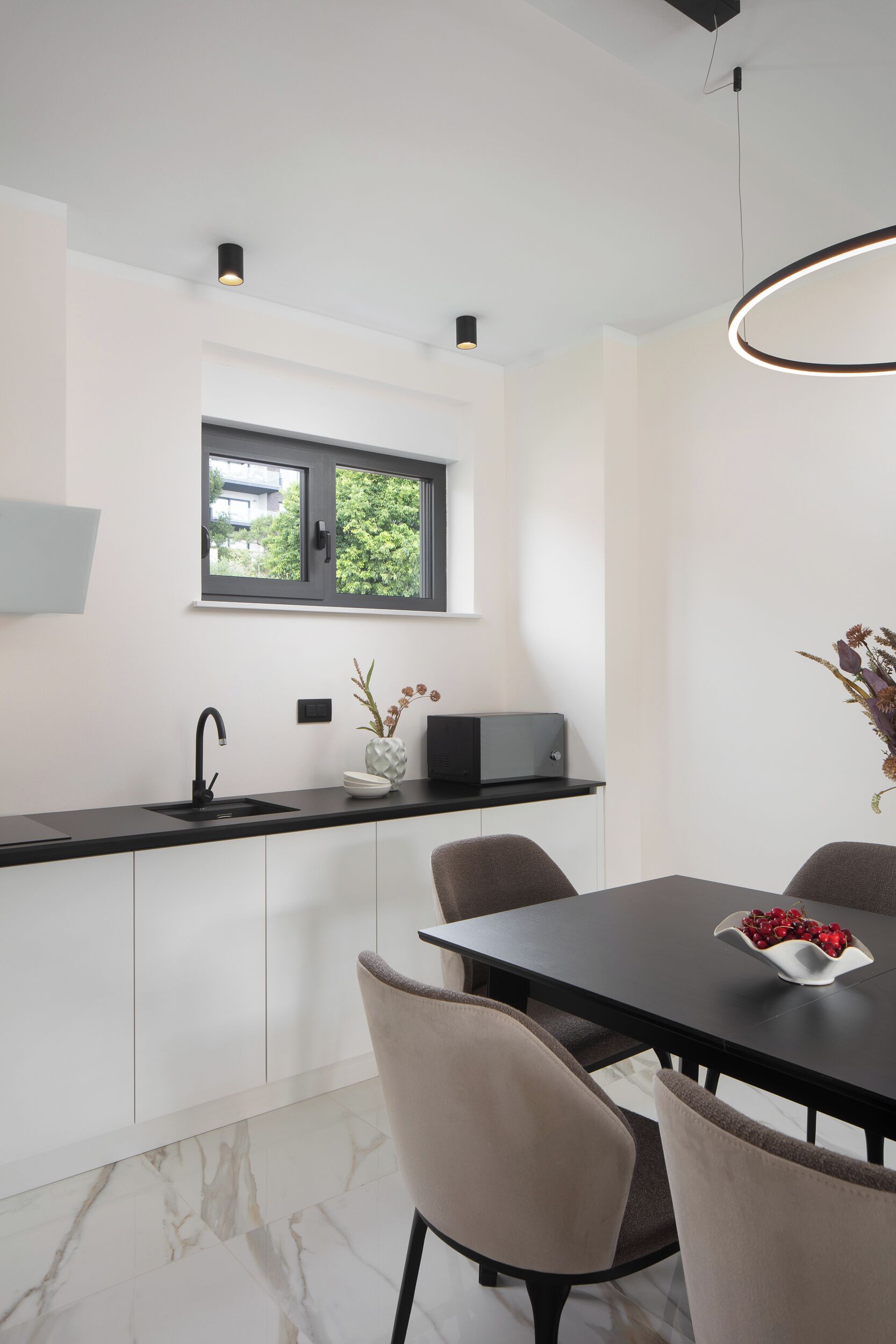 Una cocina moderna con encimera negra, armarios blancos, una ventana y un comedor con mesa y sillas.