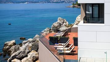 Un bâtiment moderne doté d’une terrasse donnant sur une étendue d’eau, avec des espaces de détente en plein air et une vue sur la côte.