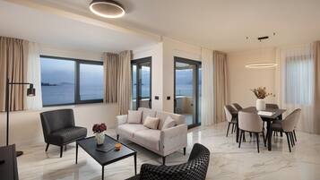 A modern living room with a sofa, chairs, a dining table, and a view of the sea.