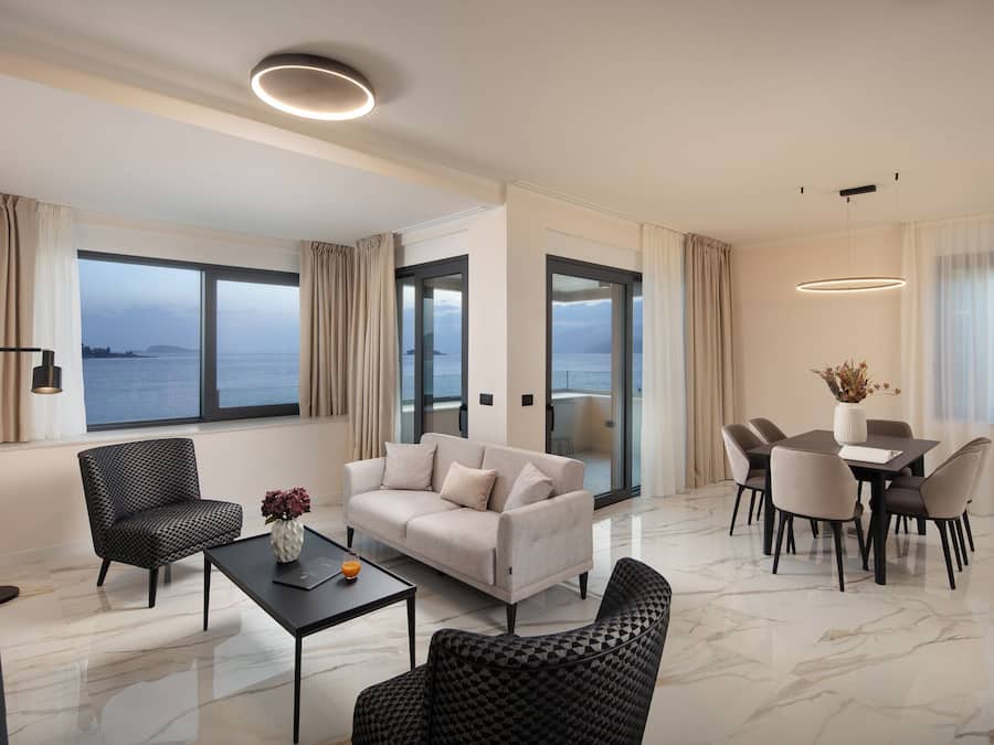 A modern living room with a sofa, chairs, a dining table, and a view of the sea.