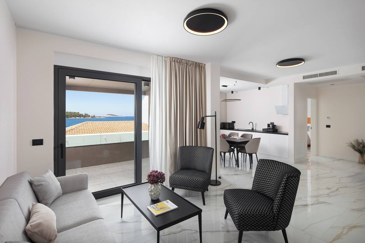 A modern living room with a sofa, armchairs, a coffee table, and a view of the sea through a large window.