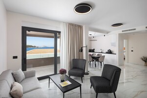 A modern living room with a sofa, armchairs, a coffee table, and a view of the sea through a large window.