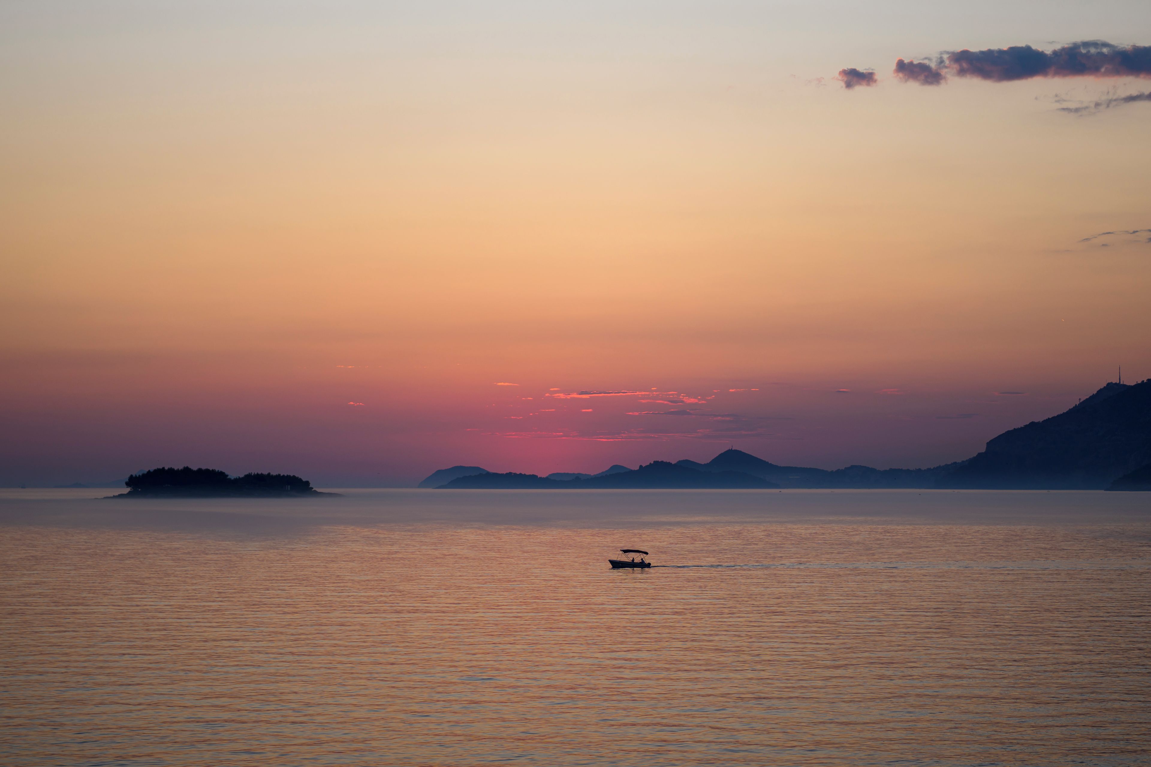 Una masa de agua tranquila con un bote en primer plano y una silueta de tierra en la lejanía contra un cielo al atardecer.