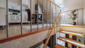 A modern kitchen with white cabinets, a marble backsplash, and a wooden staircase leading to an upper level.